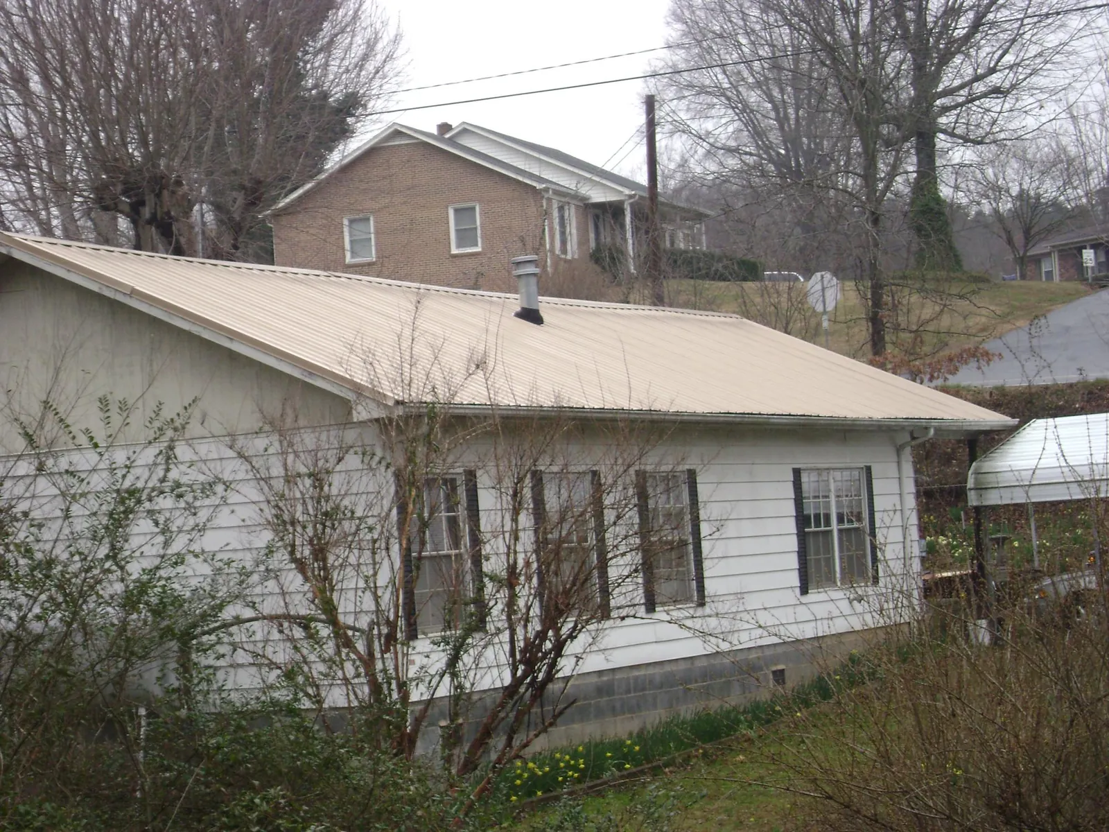 Tan metal roof on a white sided house set into a hillside — Commercial Roofing by Roofing Brothers in Pennington