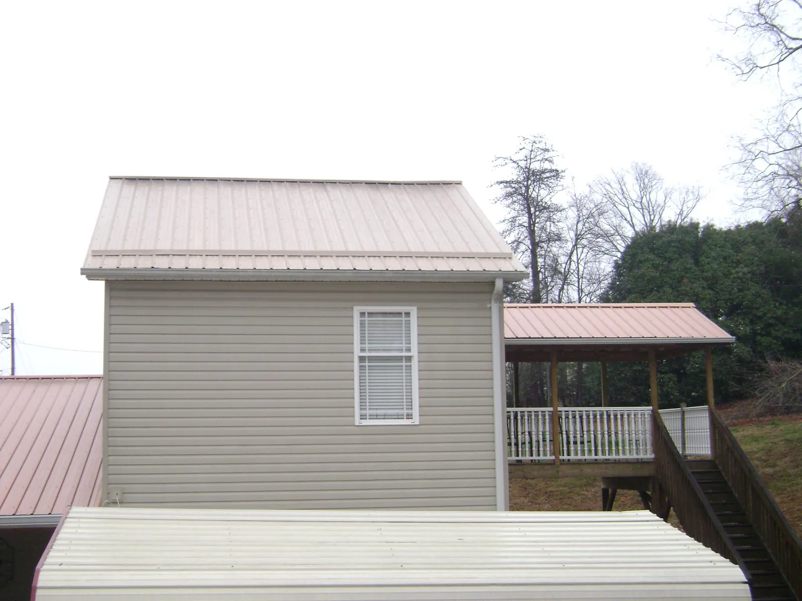 Tan metal roofs on a two story addition and attached porch, from a Roof Replacement job in Pennington